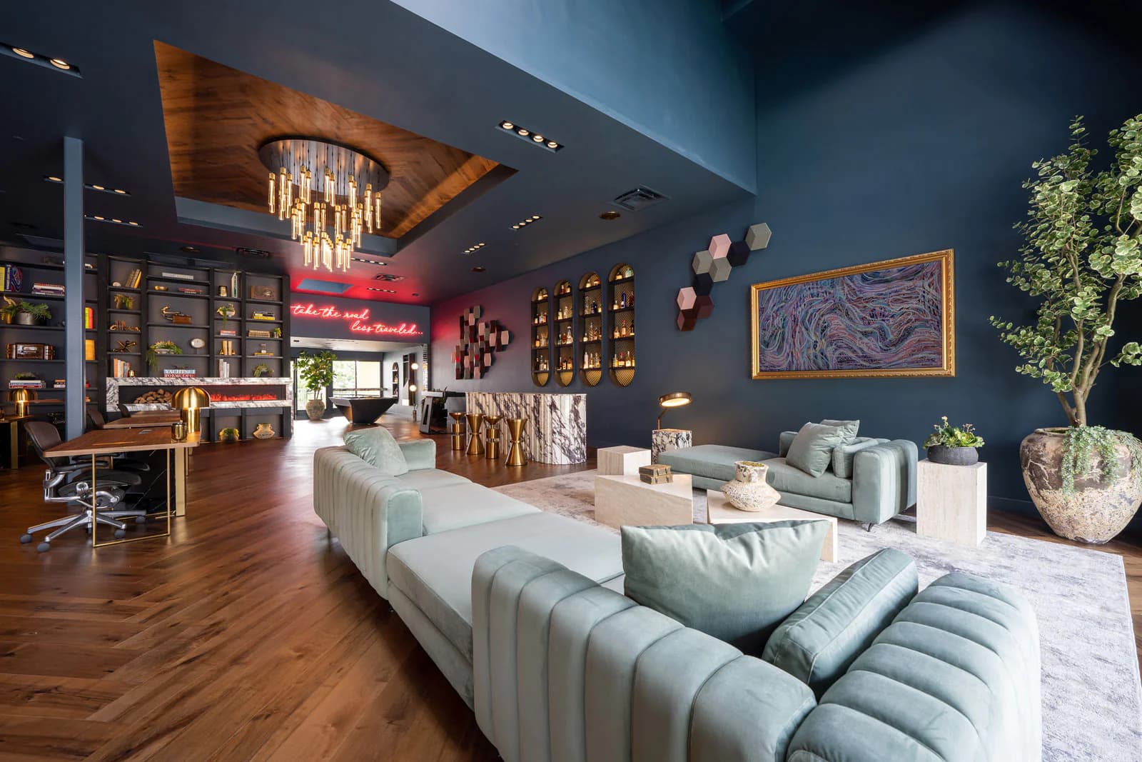 Interior of The Oppenheim Group office featuring modern decor with dark blue walls, plush light green sofas, and wooden flooring.